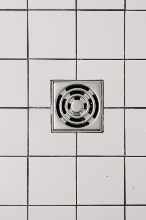 A square stainless floor waste set into white tiles