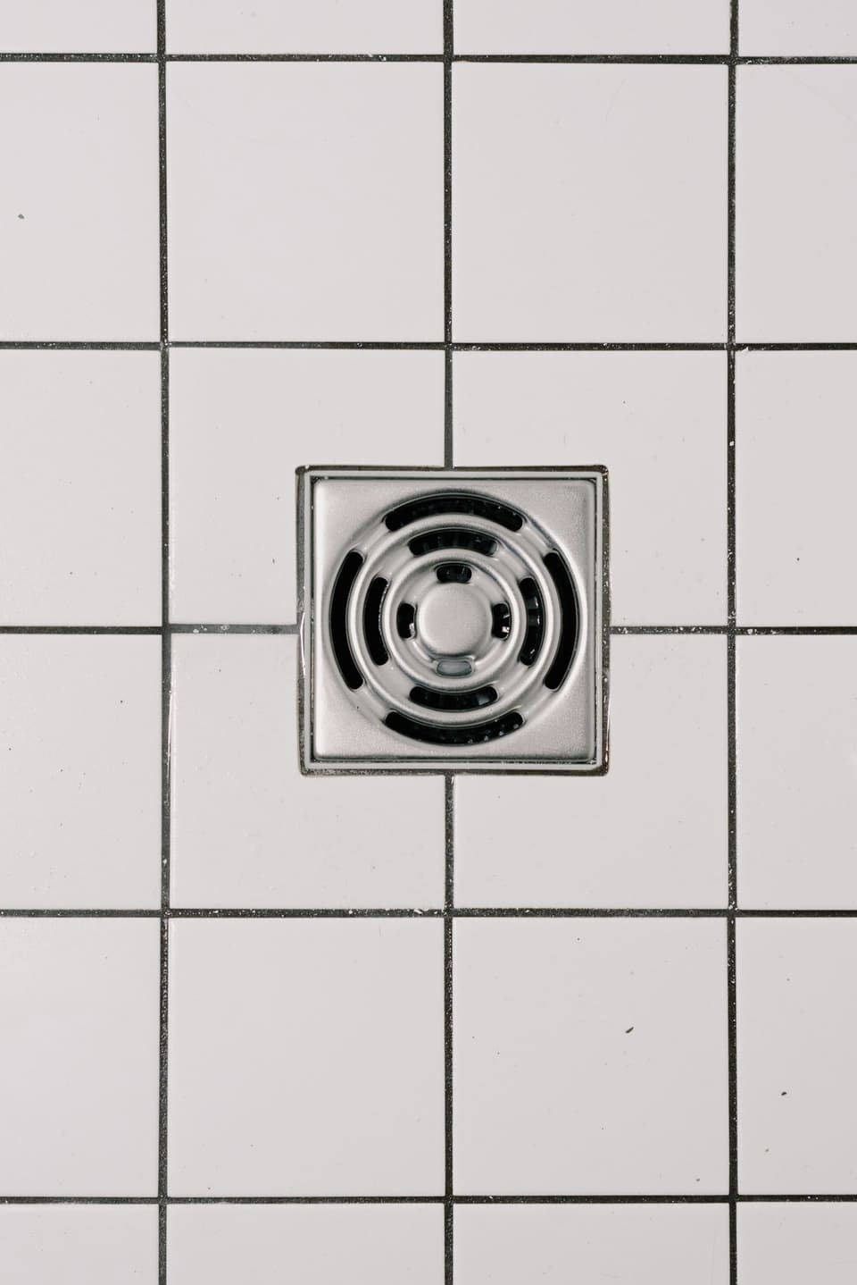 A square stainless floor waste set into white tiles