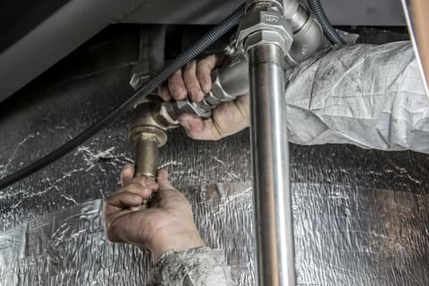 A plumber's hands tightening a fitting on a steel pipe run