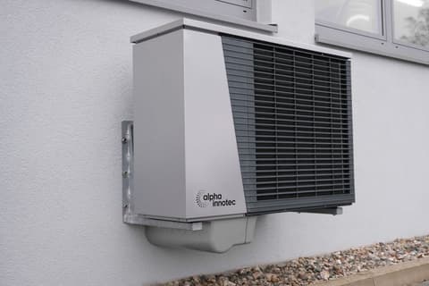 A heat pump hot water unit mounted on a rendered wall